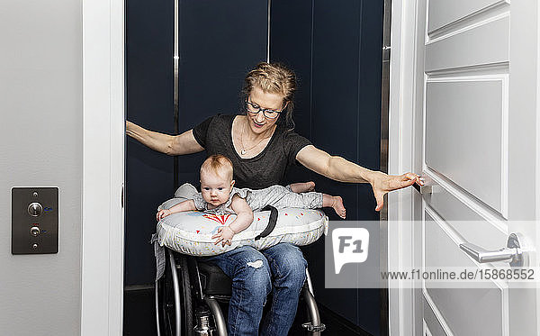 A paraplegic mother holding her baby on her lap while getting into her home elevator with her wheelchair: Edmonton  Alberta  Canada