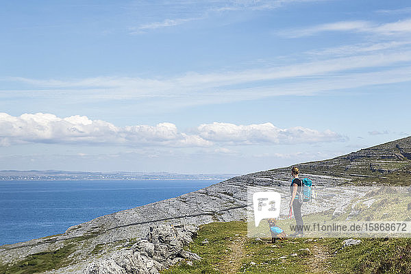 Woman and dog hiking on trail in the Burren looking out at the sea on a sunny summer day; Fanore  County Clare  Ireland