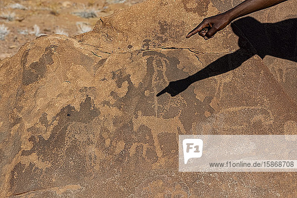 Hand und Schatten eines Mannes  die auf eine alte Felsgravurstätte zeigen  Twyfelfontein  Damaraland; Kunene-Region  Namibia