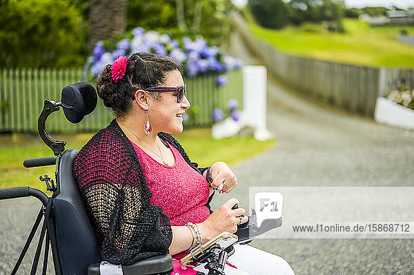 Maori woman with Cerebral Palsy in a wheelchair going down a sidewalk; Wellington  New Zealand