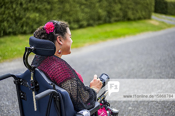 Maori woman with Cerebral Palsy in a wheelchair going down a sidewalk; Wellington New Zealand