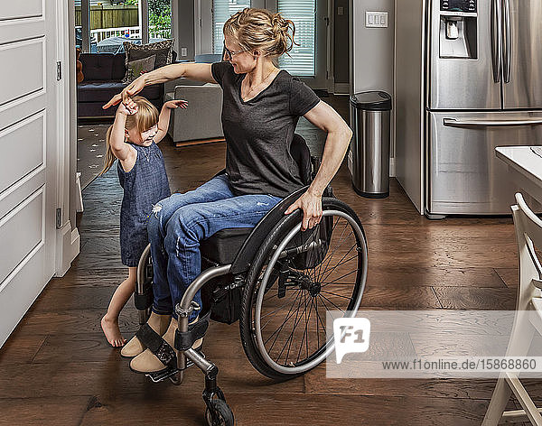 Eine querschnittsgelähmte Mutter tanzt mit ihrer Tochter in der Küche und benutzt dabei ihren Rollstuhl: Edmonton  Alberta  Kanada