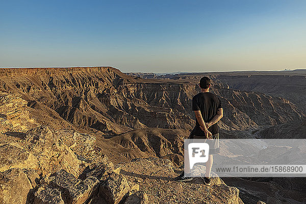 Männlicher Tourist steht auf einem Felsvorsprung mit Blick auf den Fish River Canyon; Namibia