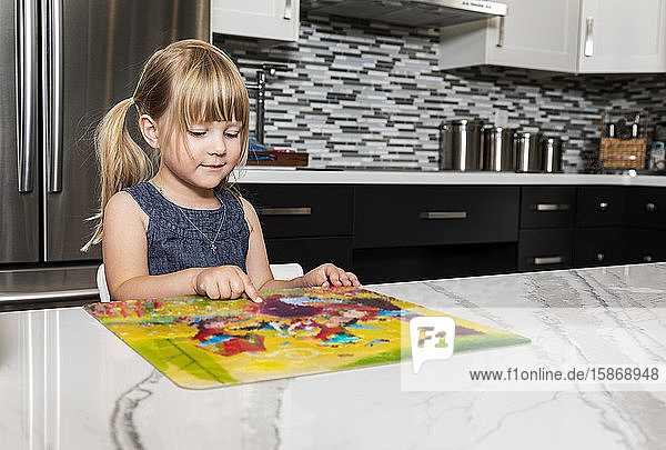 Ein süßes kleines Mädchen  das in der Küche ein Bilderbuch liest und auf etwas zeigt  das ihre Aufmerksamkeit erregt: Edmonton  Alberta  Kanada
