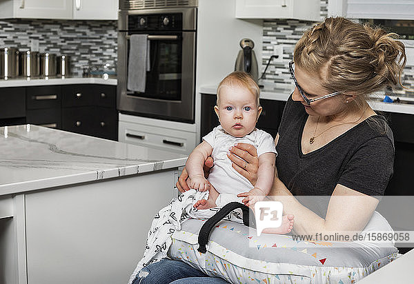 Eine querschnittsgelähmte Mutter hält ihr Baby in der Küche auf dem Schoß  während sie im Rollstuhl sitzt: Edmonton  Alberta  Kanada