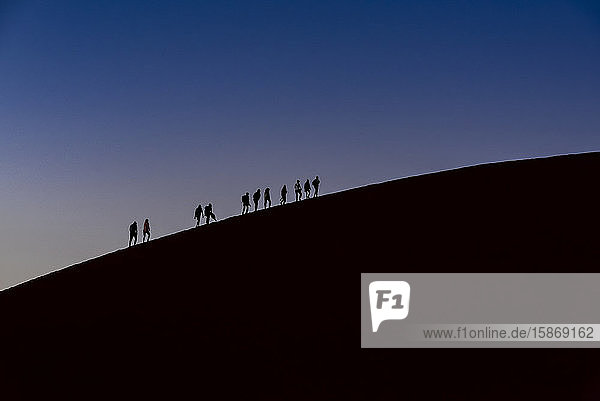 Silhouette von Touristen beim Besteigen der Düne 45 in der Abenddämmerung  Sossusvlei  Namib-Wüste; Namibia