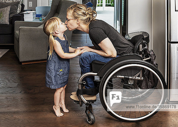 Ein junges Mädchen stellt sich auf die Zehenspitzen  um ihrer querschnittsgelähmten Mutter  die im Rollstuhl sitzt  einen Kuss zu geben: Edmonton  Alberta  Kanada.