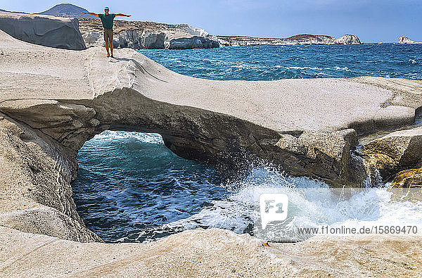 Männlicher Tourist steht auf einer einzigartigen Felsformation mit natürlichem Bogen und Brücke an der Küste der griechischen Insel Milos; Milos  Griechenland
