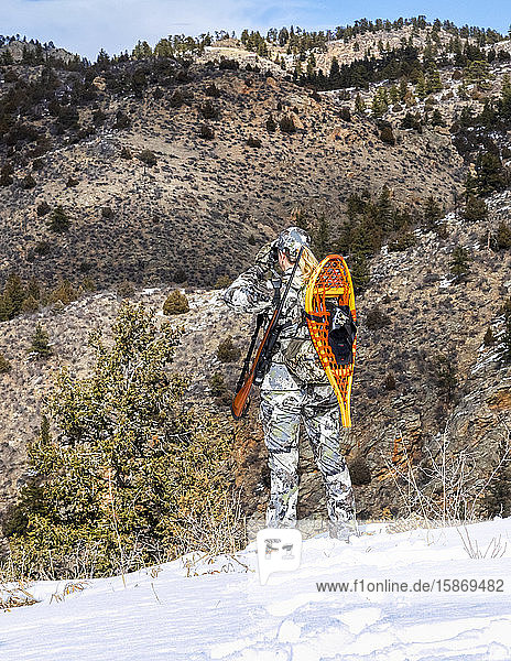 Jäger mit Tarnkleidung und Gewehr  der mit einem Fernglas im Winter nach draußen schaut; Denver  Colorado  Vereinigte Staaten von Amerika
