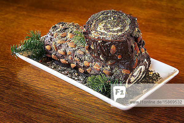 Close-up of decorative log cake with pine needle trimmings on a wooden table; Studio