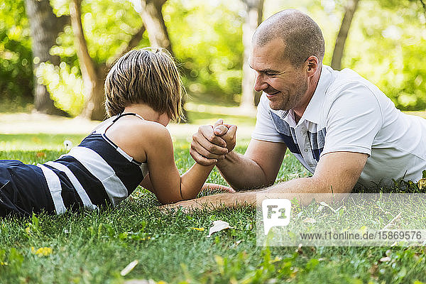 A father arm wrestling with his young daughter in a park; Edmonton  Alberta  Canada
