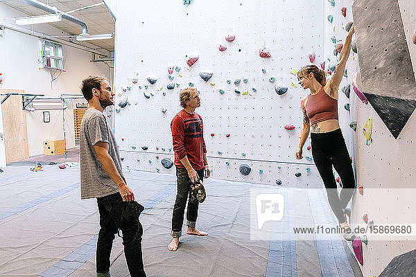 Frau klettert an der Wand  während sie den Ausbilder und den Schüler im Fitnessstudio betrachtet