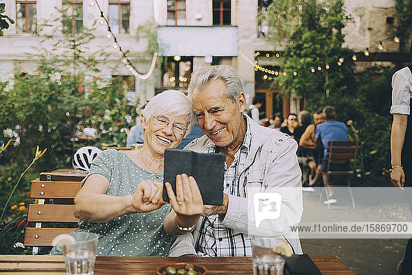 Smiling woman taking selfie with senior man while sitting at restaurant in city