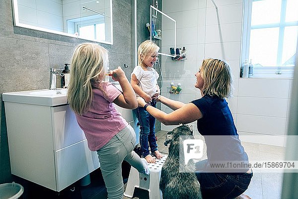 Lächelnde Mutter bindet  während ein Hund zu Hause im Badezimmer kniet