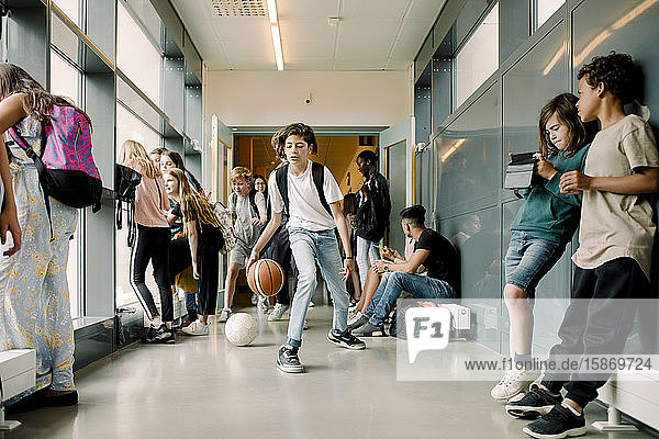Männlicher Schüler spielt in der Mittagspause auf dem Schulkorridor mit Basketball