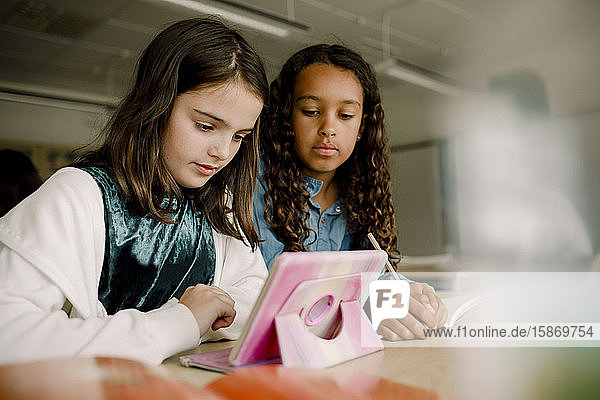 Studentinnen mit digitalem Tablett am Tisch im Klassenzimmer