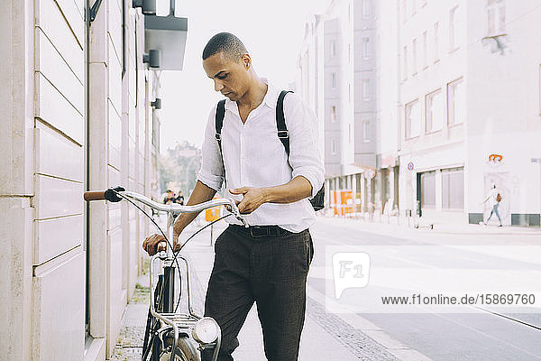 Geschäftsmann hält Fahrrad  während er in der Stadt auf dem Bürgersteig steht