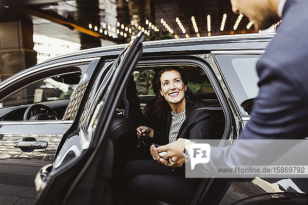 Lächelnde Unternehmerin sieht männlichen Mitarbeiter im Auto sitzend an