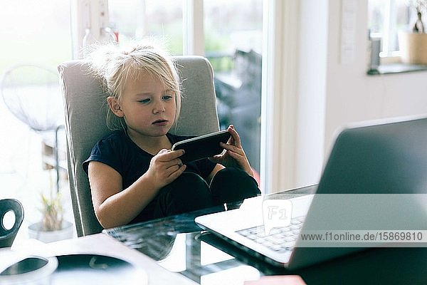 Girl surfing net in smart phone while sitting by table at home