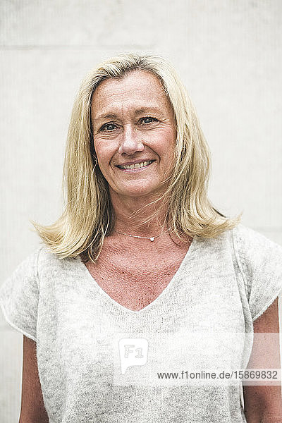 Portrait of smiling mature businesswoman standing against wall