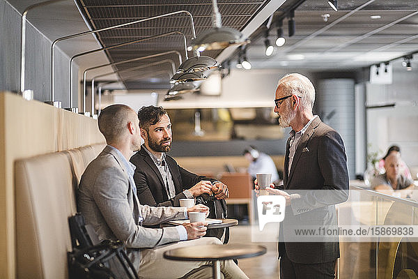 Leitender Geschäftsmann im Gespräch mit männlichen Kollegen während der Kaffeepause im Büro