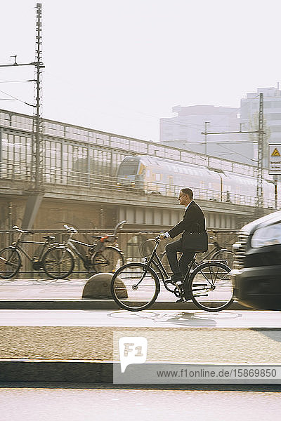 Männlicher Unternehmer fährt Fahrrad auf Straße in Stadt gegen Himmel