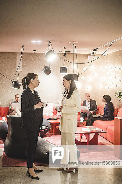 Geschäftsfrauen unterhalten sich in voller Länge in der Kaffeepause  während ihre Kollegen im Hintergrund sitzen