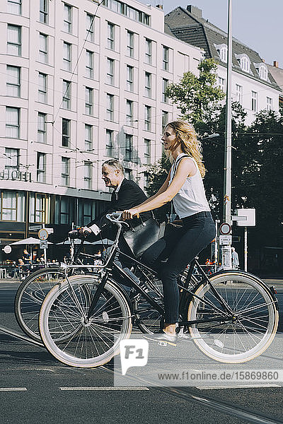 Männliche und weibliche Mitarbeiter fahren auf Straßenfahrrädern gegen Gebäude in der Stadt