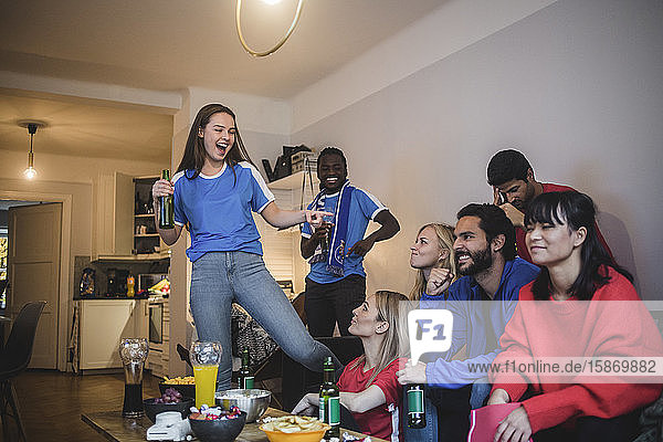 Lächelnde Frau zeigt auf Frau  während sie zu Hause mit Freunden Sport schaut