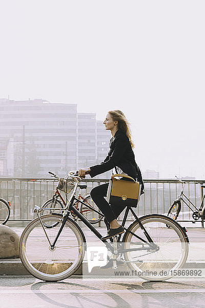 Side view of young businesswoman riding bicycle on street in city