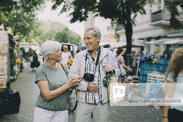 Glückliches älteres Ehepaar spricht  während es Arm in Arm auf dem Straßenmarkt geht