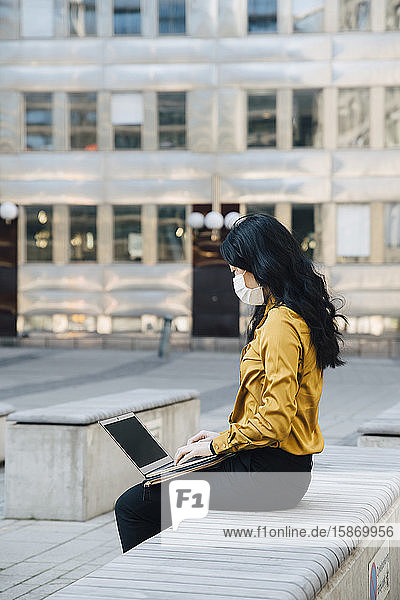 Geschäftsfrau mit Gesichtsmaske sitzt draußen und arbeitet am Laptop