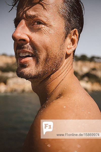 Seitenansicht eines Mannes ohne Hemd  der weg schaut  während er an einem sonnigen Tag Urlaub am Strand macht