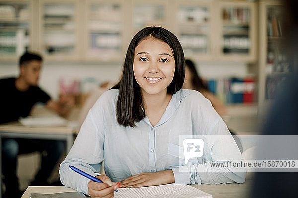 Portrait of smiling teenage girl studying at table in classroom