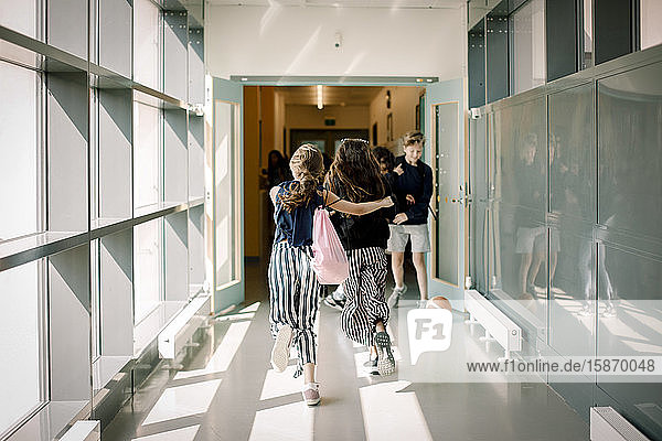 Rückansicht von Freundinnen  die auf dem Schulkorridor laufen
