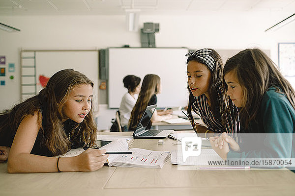 Studentinnen  die an einem Buch lernen  während sie im Klassenzimmer am Tisch sitzen