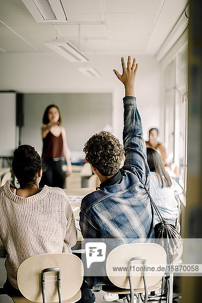 Männlicher Schüler mit erhobener Hand  während weibliche Lehrerin im Klassenzimmer auf ihn zeigt