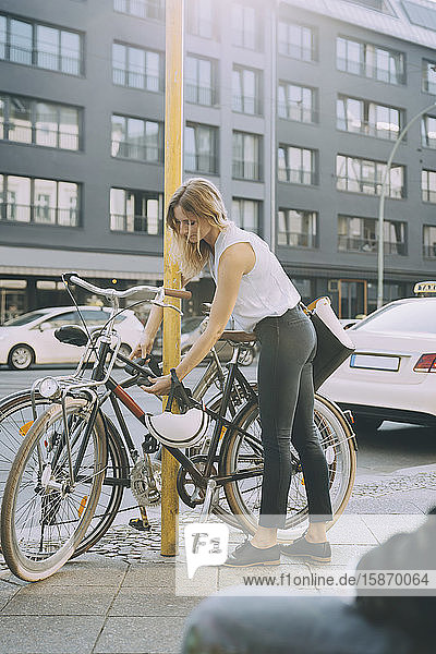 Geschäftsfrau in voller Länge sperrt Fahrrad auf Bürgersteig in der Stadt
