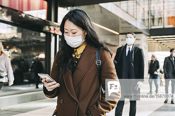 Woman with face mask walking in street using smartphone