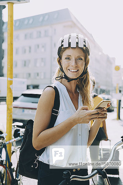 Portrait of smiling businesswoman using mobile phone while standing in city