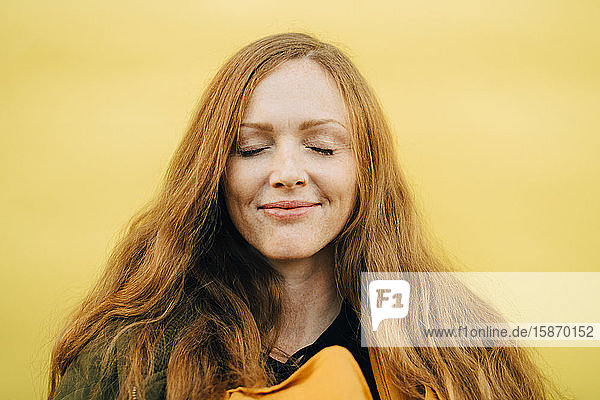Lächelnde  mittel-erwachsene Frau mit geschlossenen Augen vor gelbem Hintergrund