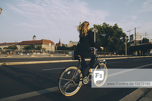 Seltener Anblick einer weiblichen Führungskraft  die in der Stadt mit dem Fahrrad auf der Straße gegen den Himmel fährt