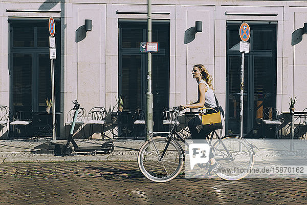 Fahrrad fahrende Geschäftsfrau in voller Länge gegen Gebäude auf der Straße in der Stadt
