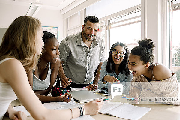 Fröhliche weibliche Teenager lernen  während die Professorin im Klassenzimmer am Tisch steht