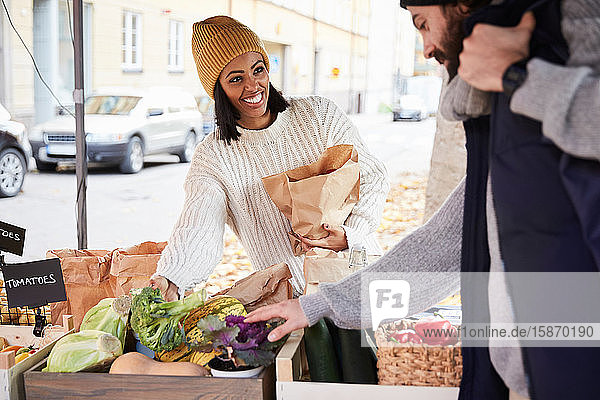 Lächelnde Frau kauft frisches Gemüse von männlichem Marktverkäufer am Obststand