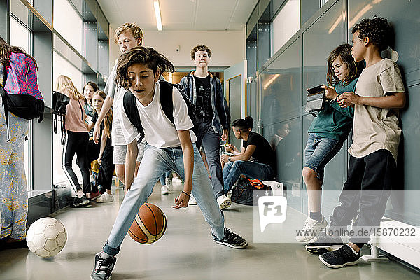 Male student playing with sports ball during lunch break in school corridor