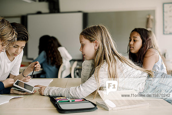 Female student pointing at digital tablet while leaning over table in classroom