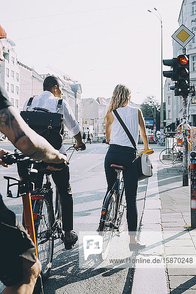 Rückansicht von Geschäftskollegen  die mit dem Fahrrad an einem Signal in der Stadt stehen