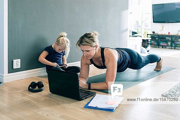 Mutter schaut auf Laptop und macht Bretter  während die Tochter im Wohnzimmer ein Smartphone benutzt