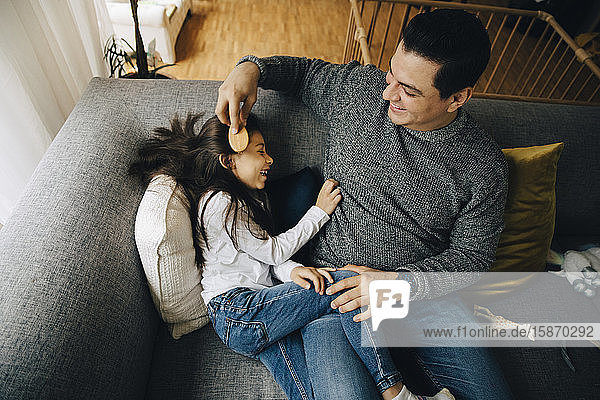 Hochwinkelansicht eines Vaters  der die Haare seiner Tochter kämmt  während er zu Hause auf dem Sofa sitzt